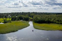 Ilmakuva rauhallisesta joesta, jota ympäröivät vehreät metsät ja niityt. Joella näkyy kumilauttailuryhmä keskellä luonnonmaisemaa.