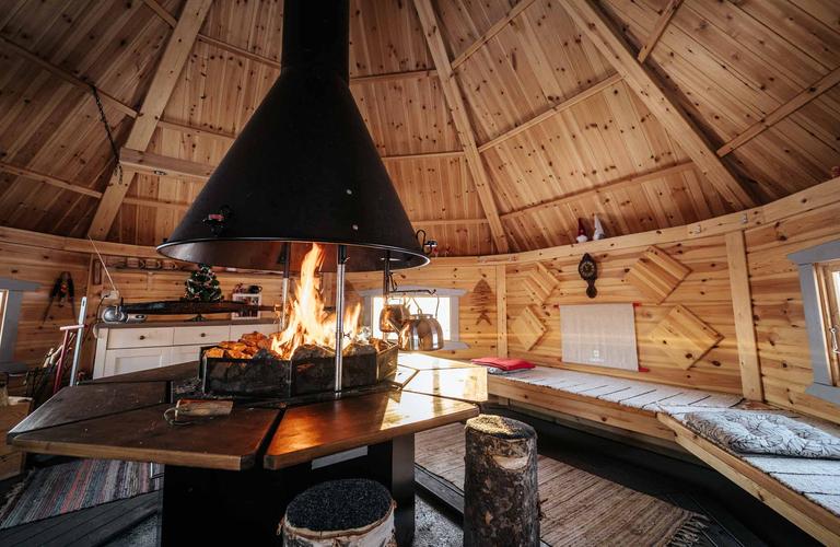 Kodikas kodan sis&auml;tila, jossa avotakka loimuaa puisen p&ouml;yd&auml;n keskell&auml;. Ymp&auml;rill&auml; on puiset penkit ja tunnelmallinen sisustus, luoden l&auml;mpim&auml;n ilmapiirin.