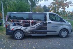 Mainoskuvioitu pakettiauto, jossa näkyy kumilauttailukuva ja yrityksen tiedot sivussa. Taustalla syksyinen metsä ja lehtipuut.