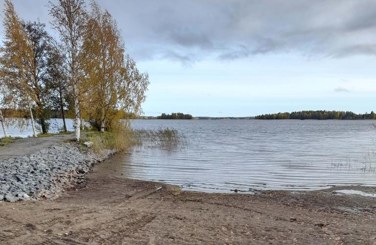 Syksyinen järvimaisema hiekkarannalla, koivupuita rannalla ja taustalla näkyviä saaria.