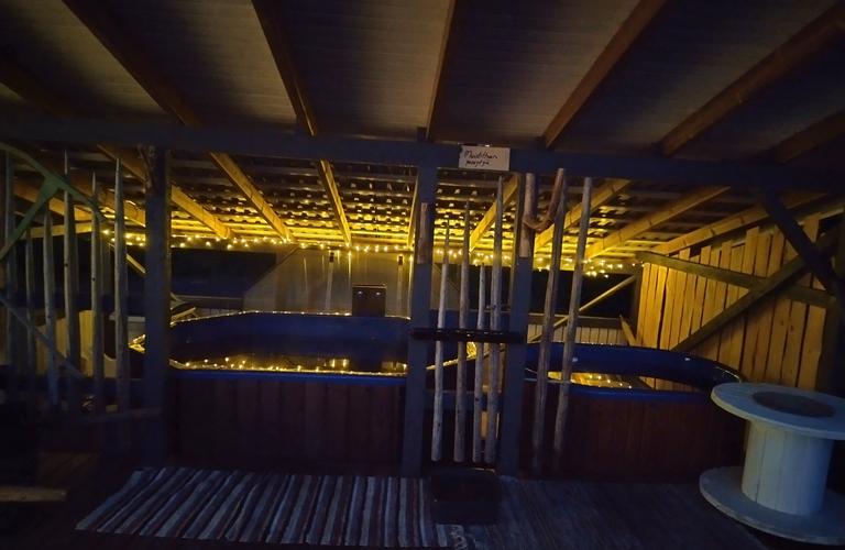 "Tunnelmallisesti valaistu palju ulkorakennuksen katoksen alla iltahämärässä. Jouluvalot luovat lämpimän ilmapiirin paljun ympärille.