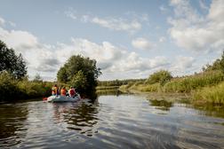 Ryhm&auml; ihmisi&auml; kelluu kumiveneell&auml; rauhallisella joella aurinkoisessa s&auml;&auml;ss&auml;, ymp&auml;rill&auml; vehreit&auml; puita ja kasvillisuutta.