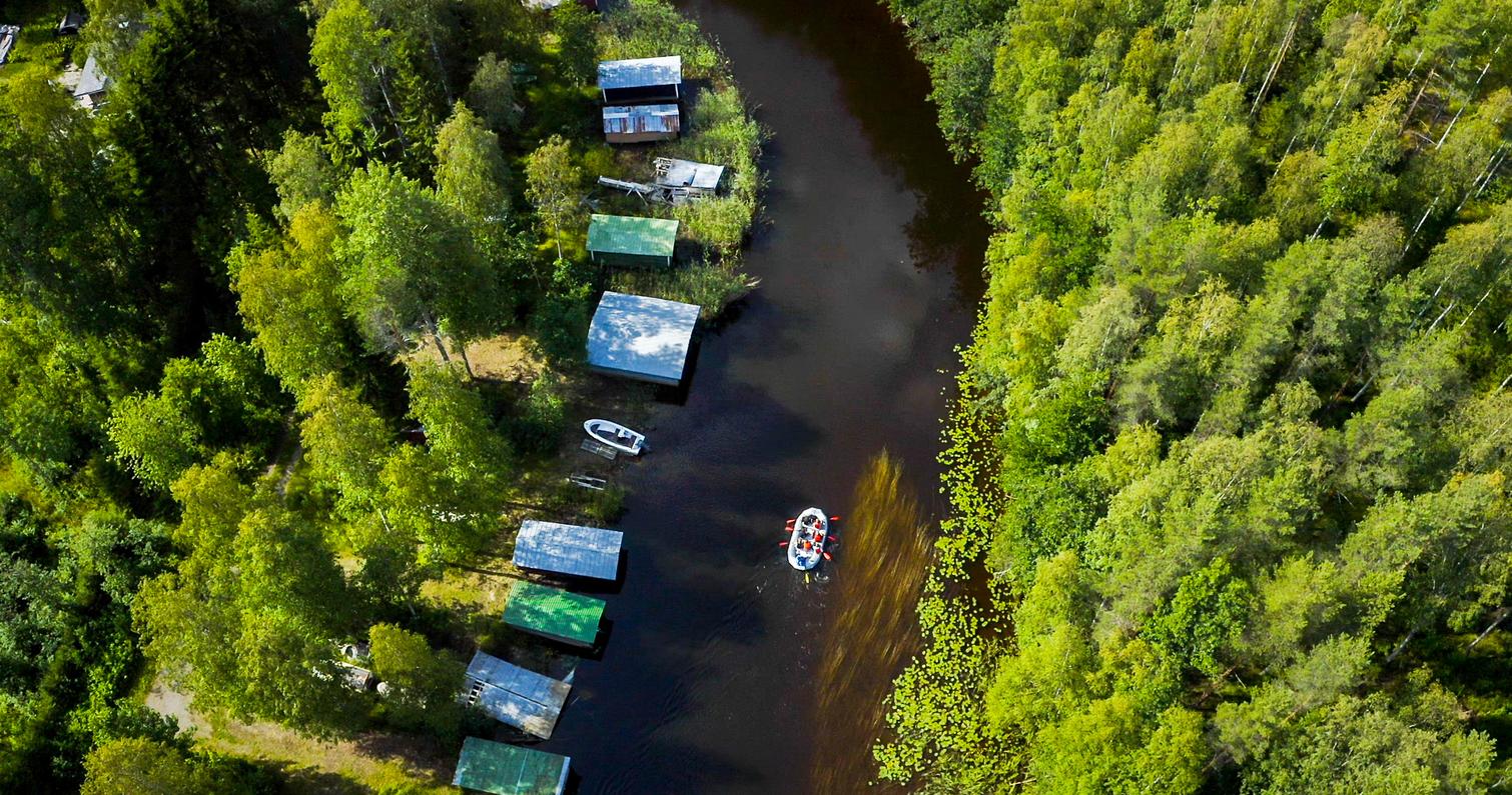 Ilmakuva kumilautasta Taipaleenjoella, jossa ryhmä meloo rauhallisesti metsäisen joen varrella, venevajoja näkyy joen rannassa.