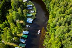 Ilmakuva kumilautasta Taipaleenjoella, jossa ryhm&auml; meloo rauhallisesti mets&auml;isen joen varrella, venevajoja n&auml;kyy joen rannassa.